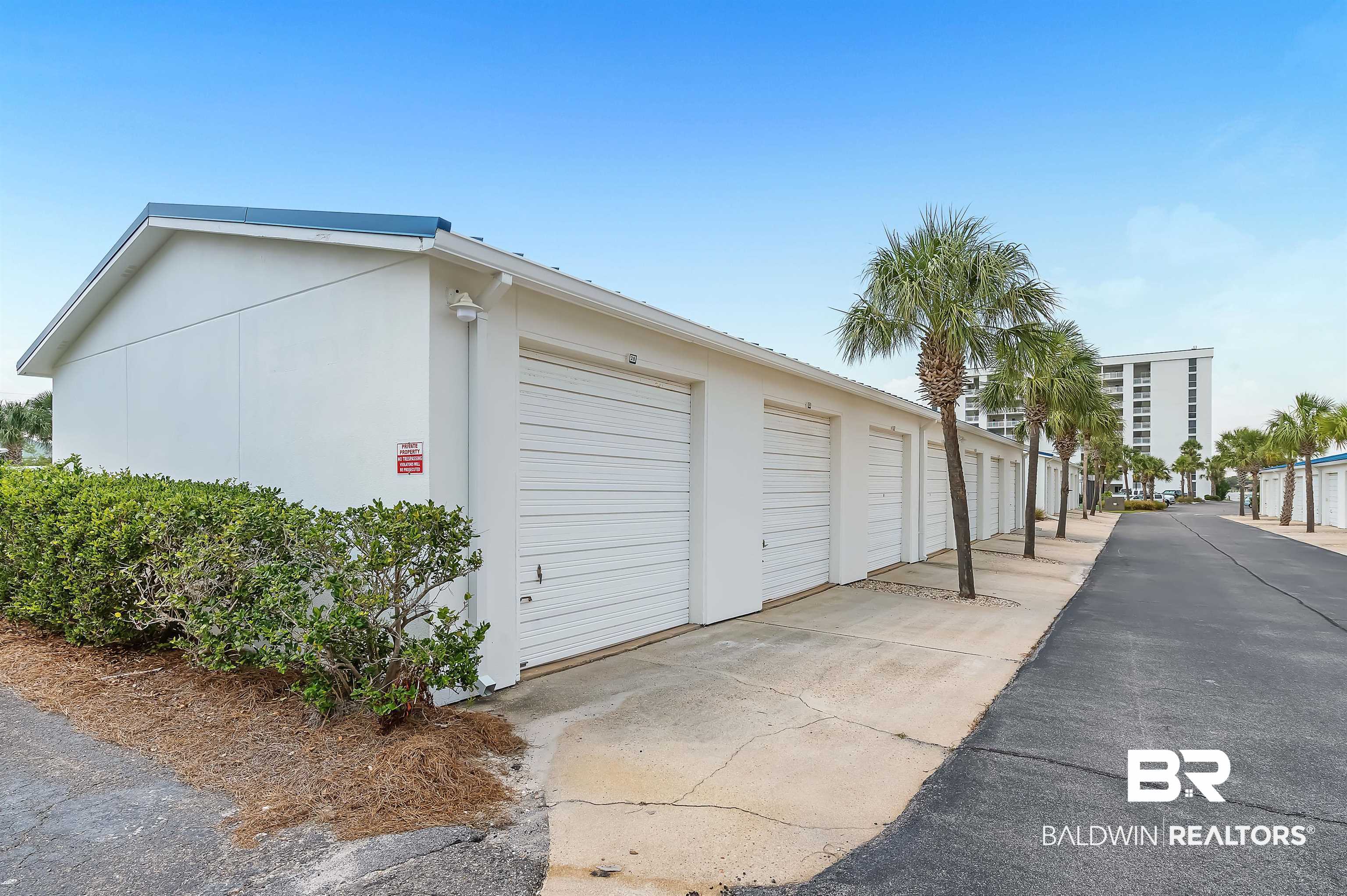 16287 Perdido Key Drive, Unit 105 Pensacola, FL 32507 - Photo 56 of 66 White stucco exterior with multiple individual garage units featuring roll-up doors, concrete driveways, and surrounding landscaping
