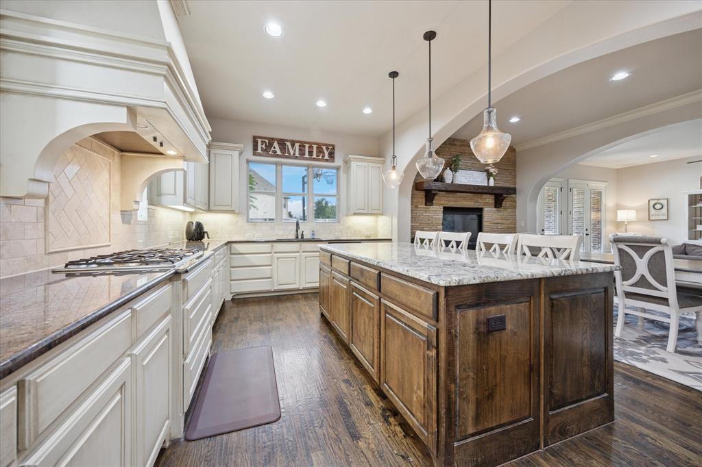 580 Butchart Drive Prosper, TX 75078 - Photo 40 of 40 Kitchen featuring stainless steel gas cooktop, open floor plan, dark wood finished floors, light stone countertops, and a kitchen island