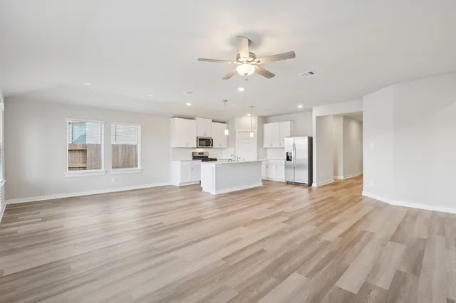 a view of an empty room with wooden floor and a kitchen