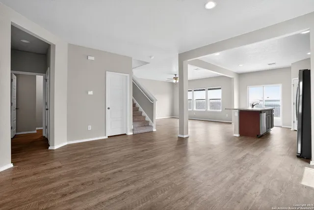 a view of an empty room with wooden floor and a kitchen