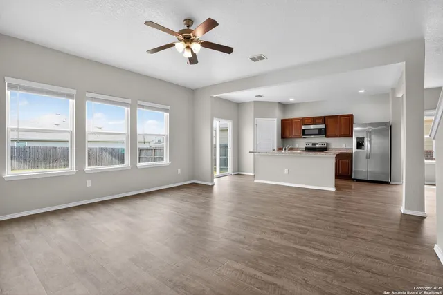 a view of an empty room with kitchen and window