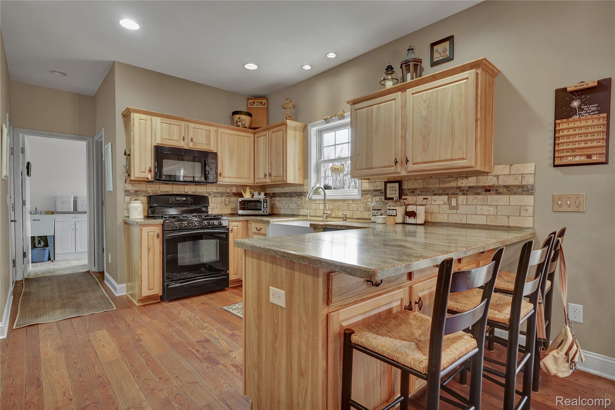 3690 Brauer Road Oxford, MI 48371 - Photo 19 of 63 Kitchen featuring light wood finish cabinets, a peninsula, black appliances, a kitchen bar, and light wood finished floors
