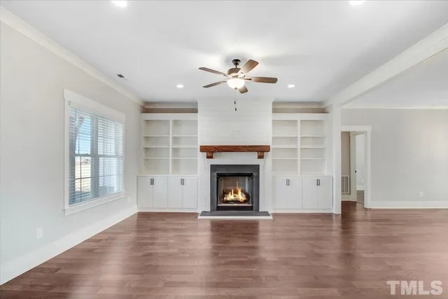 an empty room with wooden floor fire place and kitchen view