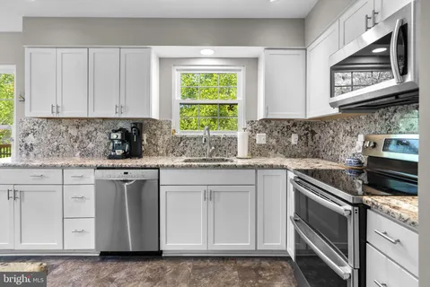 a kitchen with stainless steel appliances granite countertop white cabinets sink and window