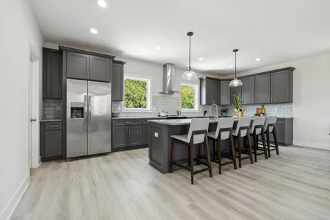 a kitchen with stainless steel appliances granite countertop a refrigerator a sink dishwasher a stove and a dining table with wooden floor