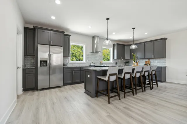 a kitchen with stainless steel appliances granite countertop a refrigerator a sink dishwasher a stove and a dining table with wooden floor