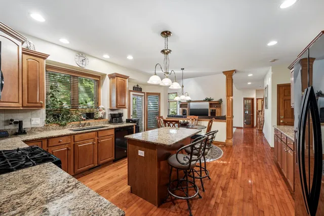a kitchen with stainless steel appliances granite countertop a sink dishwasher a refrigerator and a dining table with wooden floor