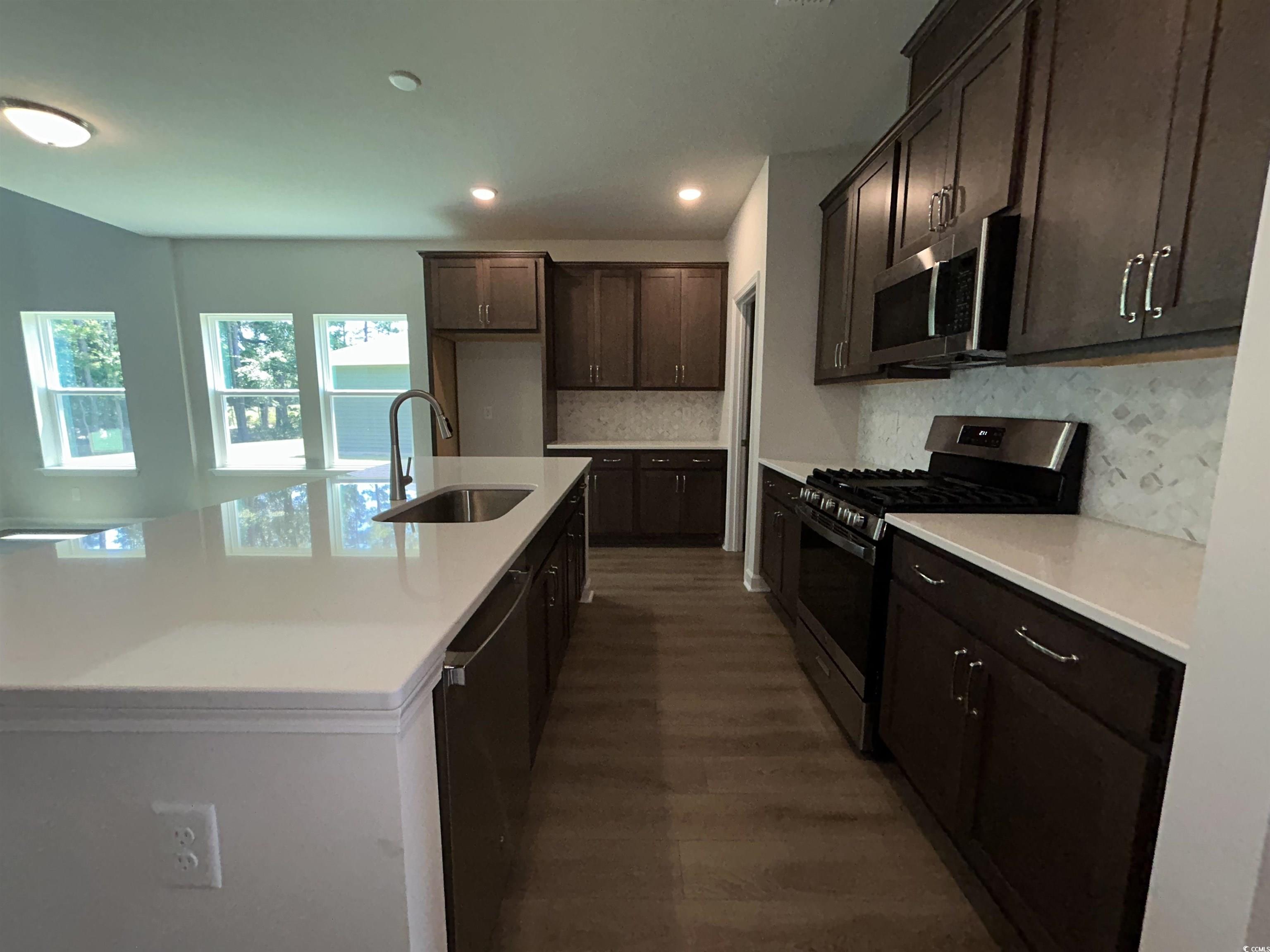 3068 Palma Way Myrtle Beach, SC 29579 - Photo 13 of 30 Kitchen featuring appliances with stainless steel finishes, dark wood finished floors, dark brown cabinetry, decorative backsplash, and an island with sink