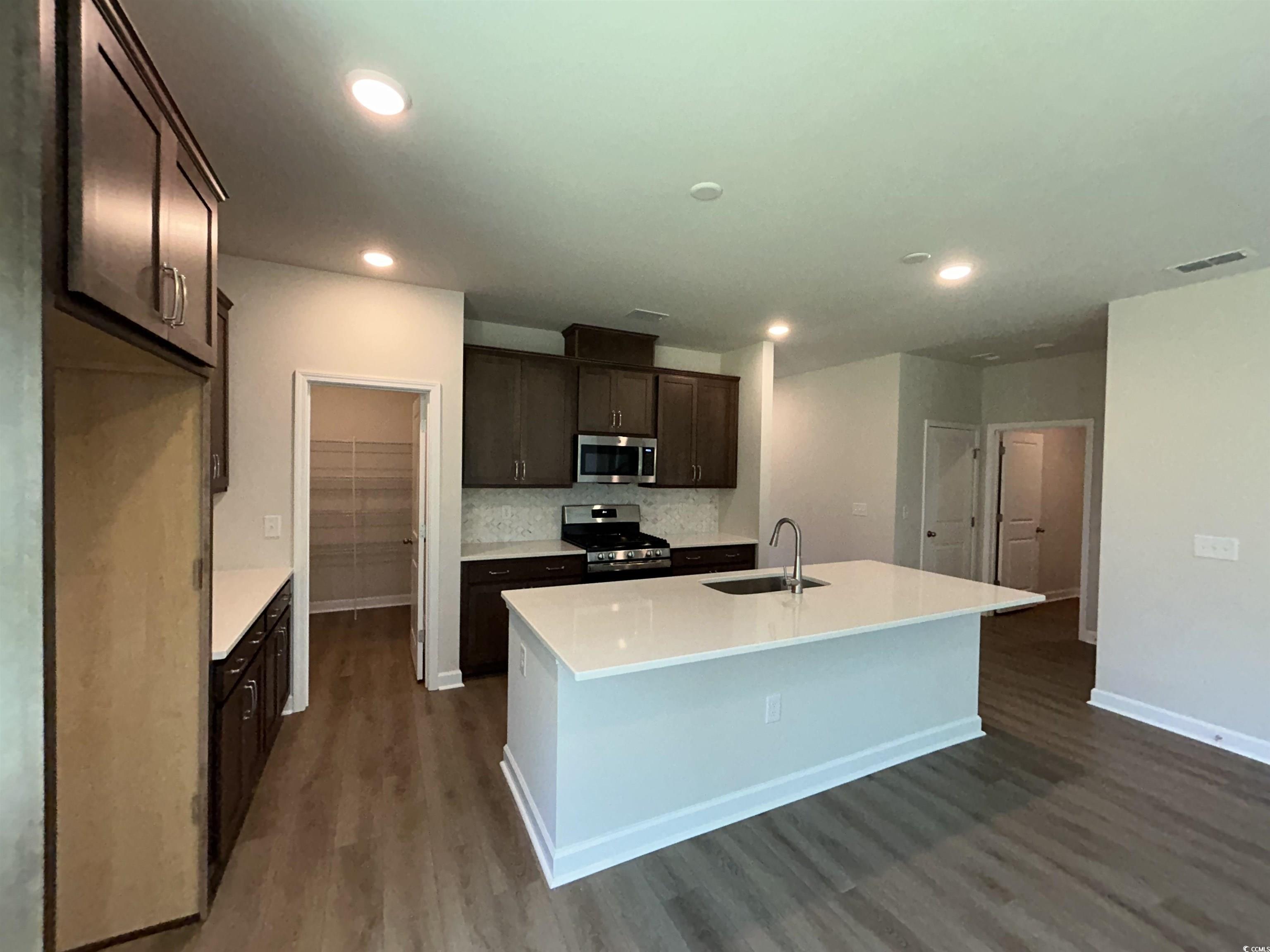 3068 Palma Way Myrtle Beach, SC 29579 - Photo 15 of 30 Kitchen featuring appliances with stainless steel finishes, dark wood finished floors, dark brown cabinets, a kitchen island with sink, and recessed lighting
