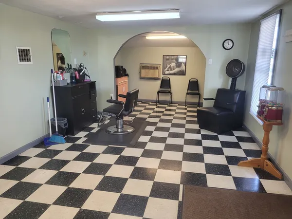 a living room with a black white checkered floor with a gaming machine and dining chairs