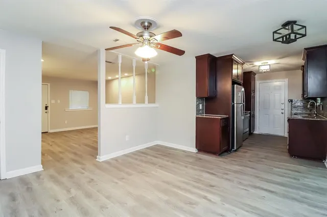 an empty room with wooden floor and way to kitchen