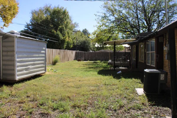 a view of a backyard with large trees and wooden fence