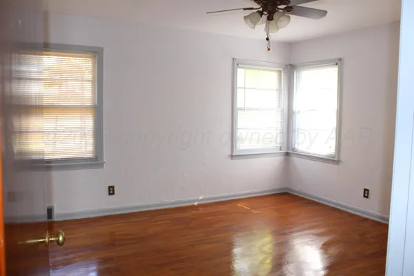 a view of an empty room with wooden floor and fan