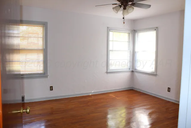 a view of an empty room with wooden floor and fan