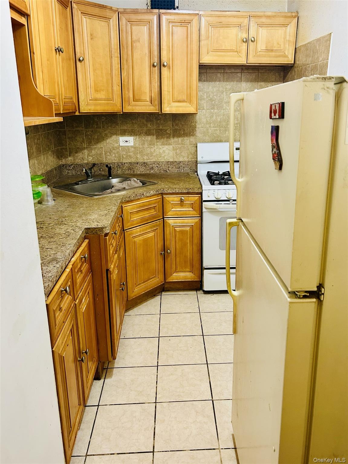 89-00 170th Street, Unit 6G Queens, NY 11432 - Photo 3 of 9 Kitchen with white appliances, light tile patterned floors, brown cabinetry, backsplash, and light countertops