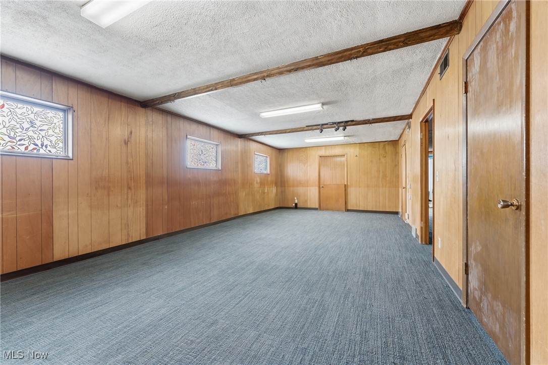 1817 Fulton Road Northwest Canton, OH 44709 - Photo 11 of 25 Unfurnished room with a textured ceiling, wooden walls, healthy amount of natural light, and dark colored carpet