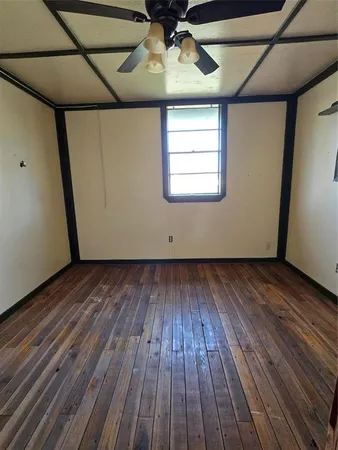 a view of an empty room with wooden floor and a ceiling fan