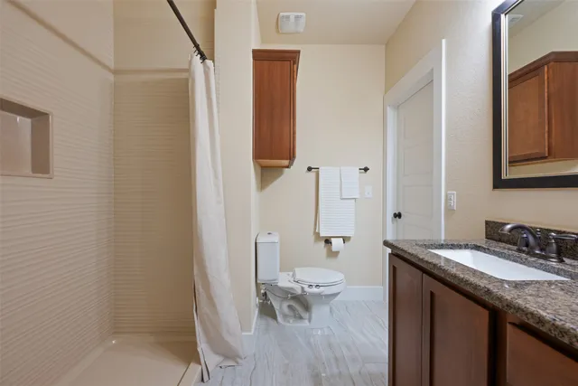 a bathroom with a granite countertop sink a toilet a mirror and shower