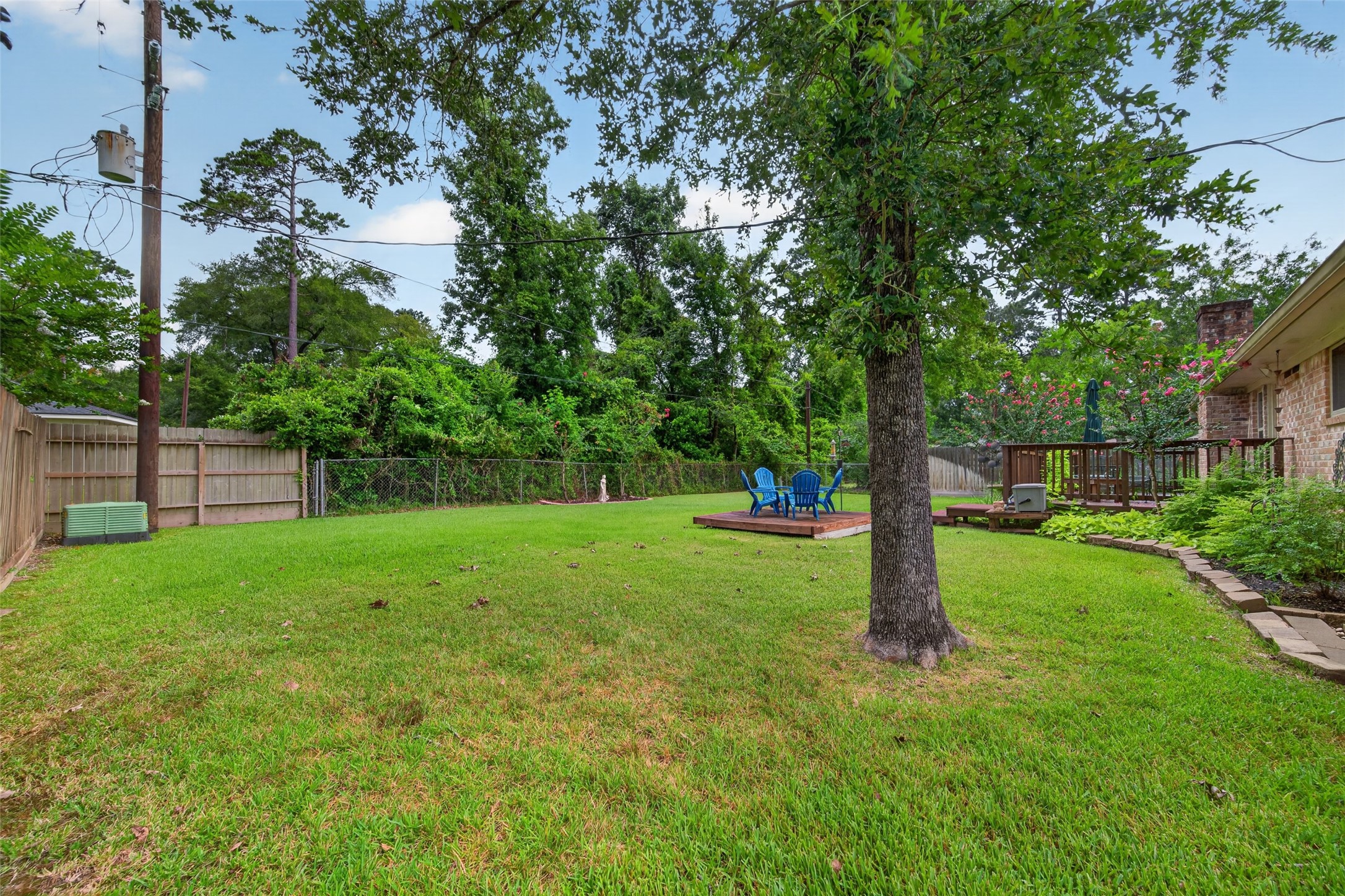 24719 Wilderness Road Spring, TX 77380 - Photo 39 of 42 This photo showcases a spacious backyard featuring a lush green lawn, a mature tree, and a wooden deck area. The area is enclosed by a wooden fence, providing privacy and a serene outdoor space ideal for relaxation or entertaining.
