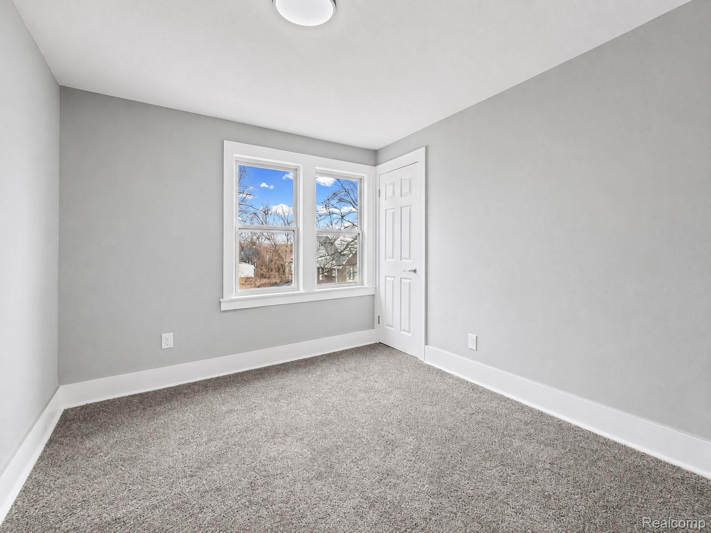 9175 Devonshire Road Detroit, MI 48224 - Photo 13 of 23 Carpeted room featuring a white paneled door, dual windows with white trim, a flush-mount ceiling light, and light gray painted walls with white baseboards