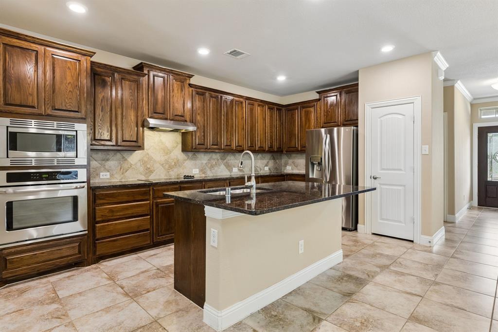 537 Hunt Farms Road Fate, TX 75189 - Photo 9 of 36 Kitchen featuring dark wood cabinetry, stainless steel appliances, a center island with a sink, stone countertops, and tile flooring