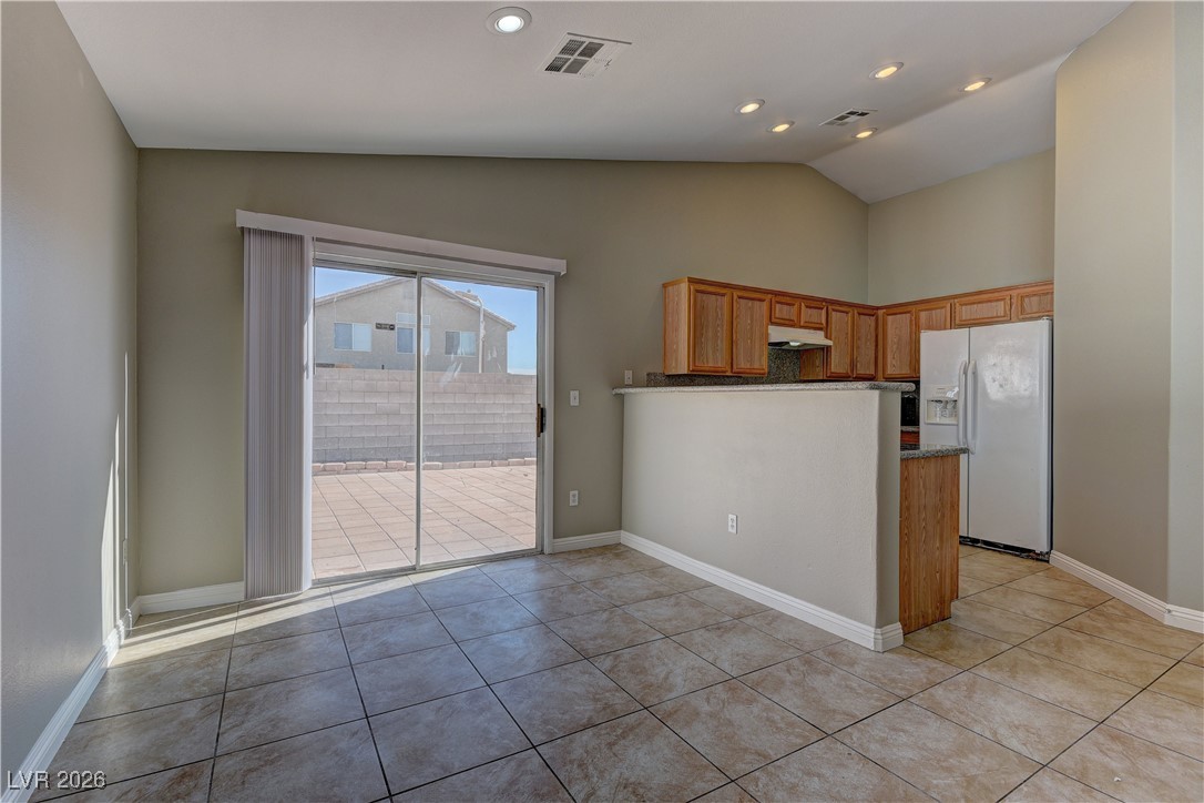 3328 Strawberry Roan Road North Las Vegas, NV 89032 - Photo 5 of 11 Kitchen featuring white refrigerator with ice dispenser, brown cabinets, lofted ceiling, a peninsula, and light tile patterned floors