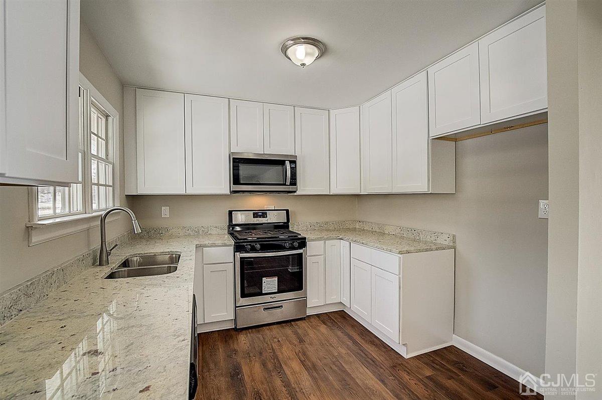 17 Cambridge Road Kendall Park, NJ 08824 - Photo 13 of 28 a kitchen with stainless steel appliances a stove a sink cabinets and a wooden floor