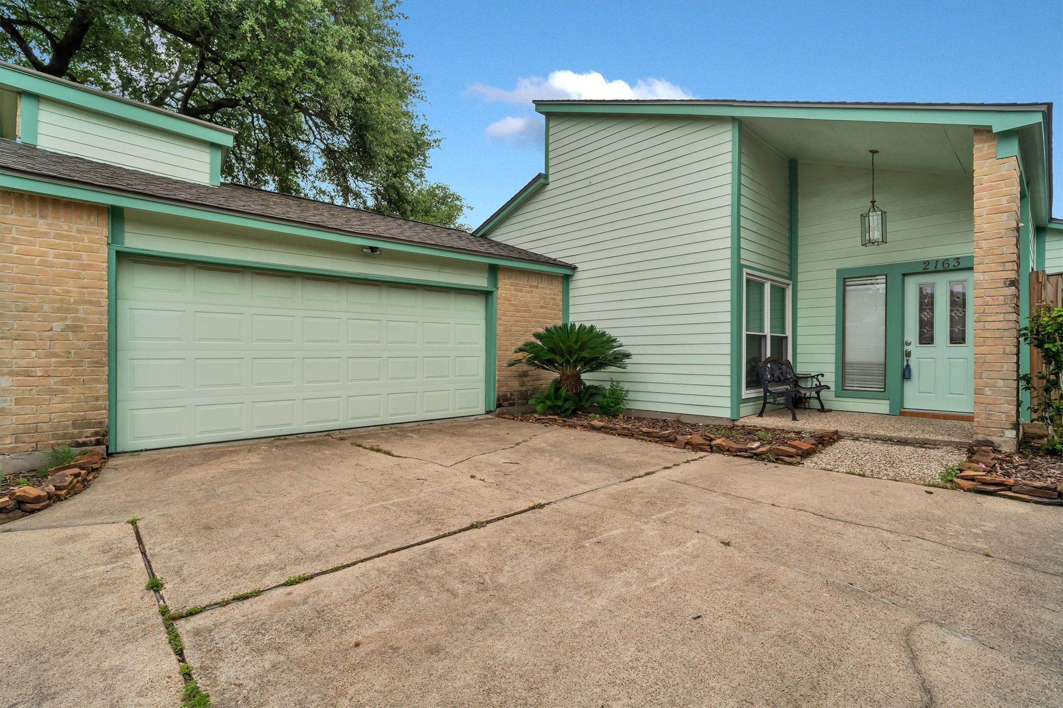 2163 Paso Rello Drive Houston, TX 77077 - Photo 1 of 45 Home features a welcoming front entrance with a modern design, double garage, and a cozy front porch. The exterior is accented with soft green tones and brick, offering a charming curb appeal.