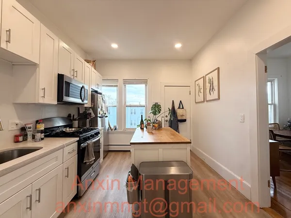 a kitchen with stainless steel appliances granite countertop a stove top oven a sink a refrigerator white cabinets and wooden floor