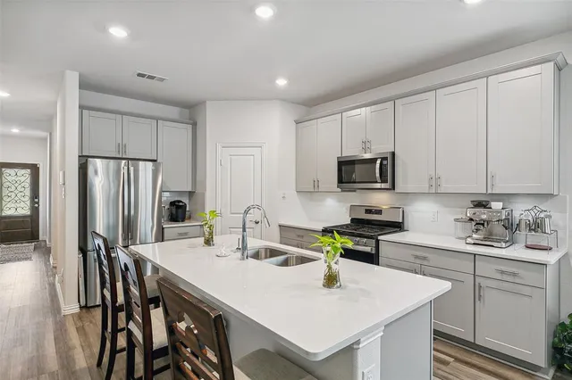 a kitchen with stainless steel appliances granite countertop a sink a microwave a stove a refrigerator and white cabinets with wooden floor