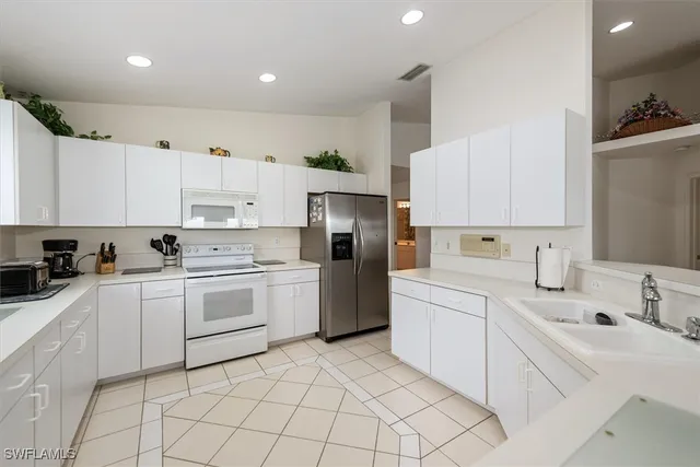 a kitchen with stainless steel appliances granite countertop a sink a stove a refrigerator and white cabinets with wooden floor