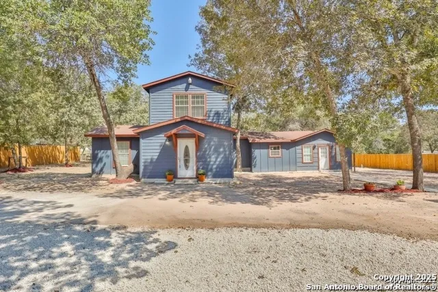 a front view of a house with a dirt yard and a large tree