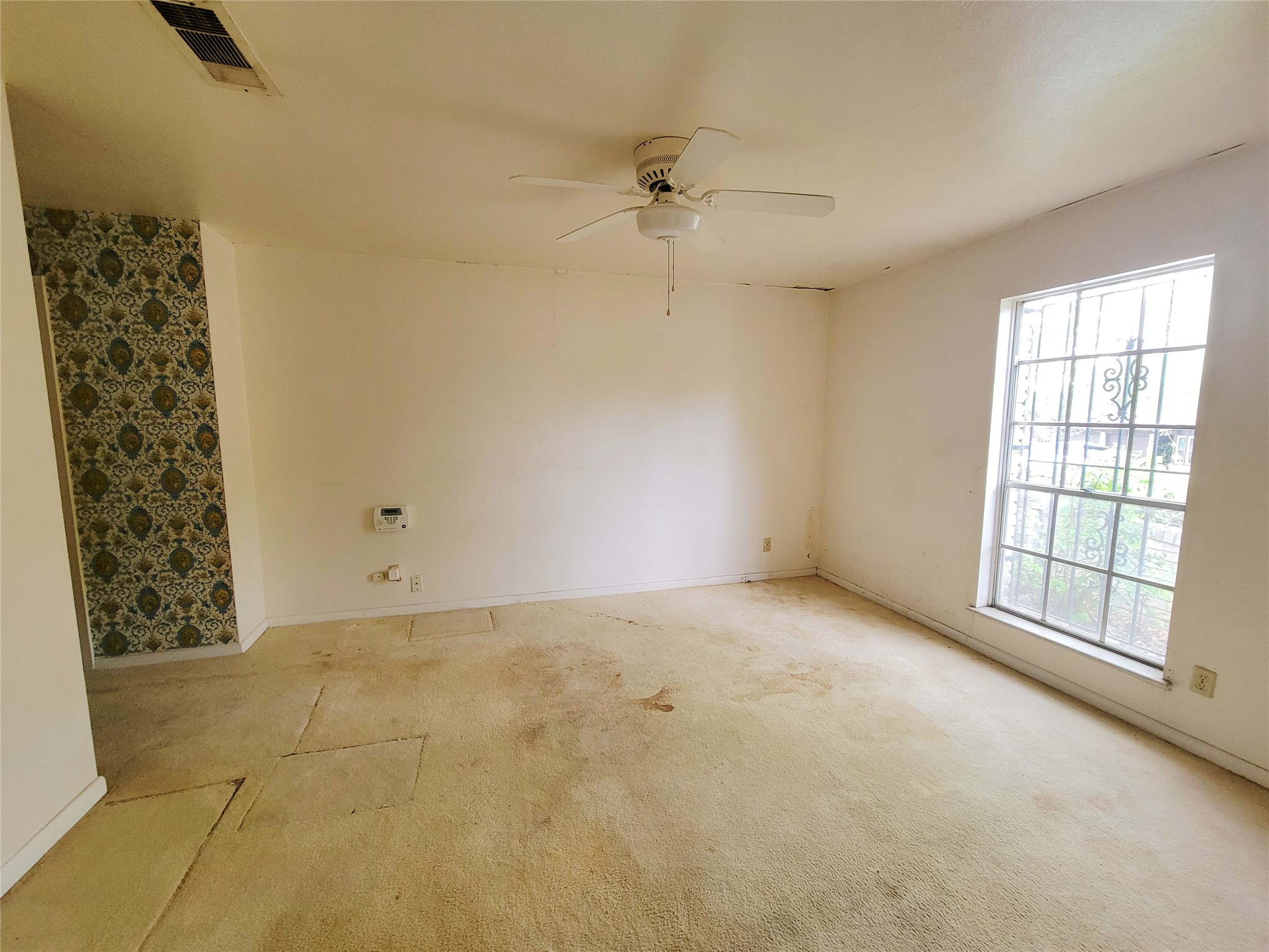 6605 Highpoint Drive Austin, TX 78723 - Photo 7 of 11 Spacious room featuring a ceiling fan, a large window with security bars, and an accent wall with patterned wallpaper