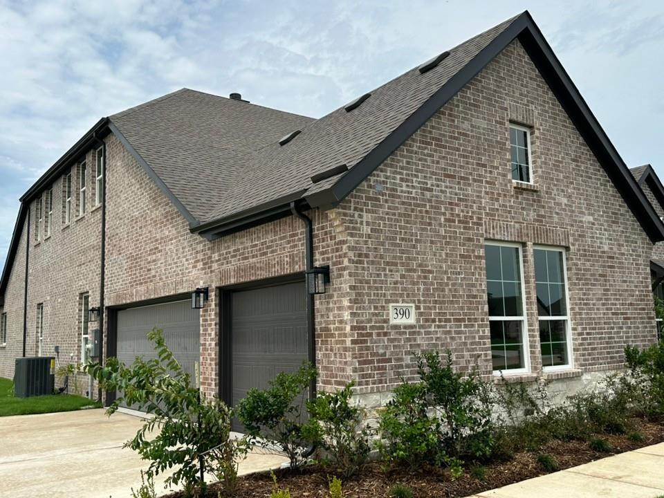 390 Cobb Road Leonard, TX 75452 - Photo 3 of 26 Brick exterior featuring dark gray garage doors, black gutters, and a prominent gable roofline