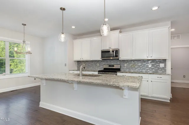 a large kitchen with granite countertop a stove a sink a center island and cabinets