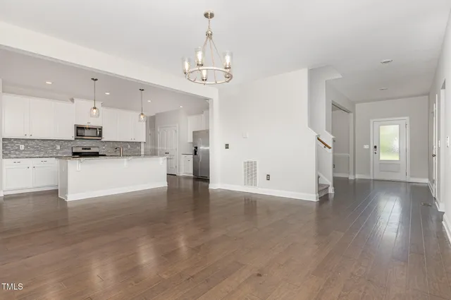 a view of an empty room and kitchen with wooden floor