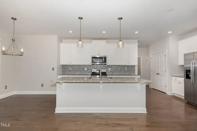 a large kitchen with stainless steel appliances granite countertop a sink a refrigerator a stove a oven and a wooden floor