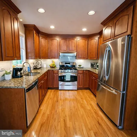 a kitchen with granite countertop wooden floors stainless steel appliances a sink and a window