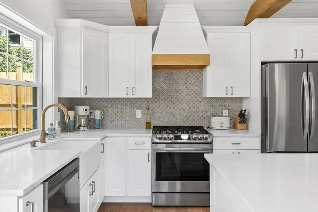 a kitchen with stainless steel appliances a stove a sink a refrigerator white cabinets and a window