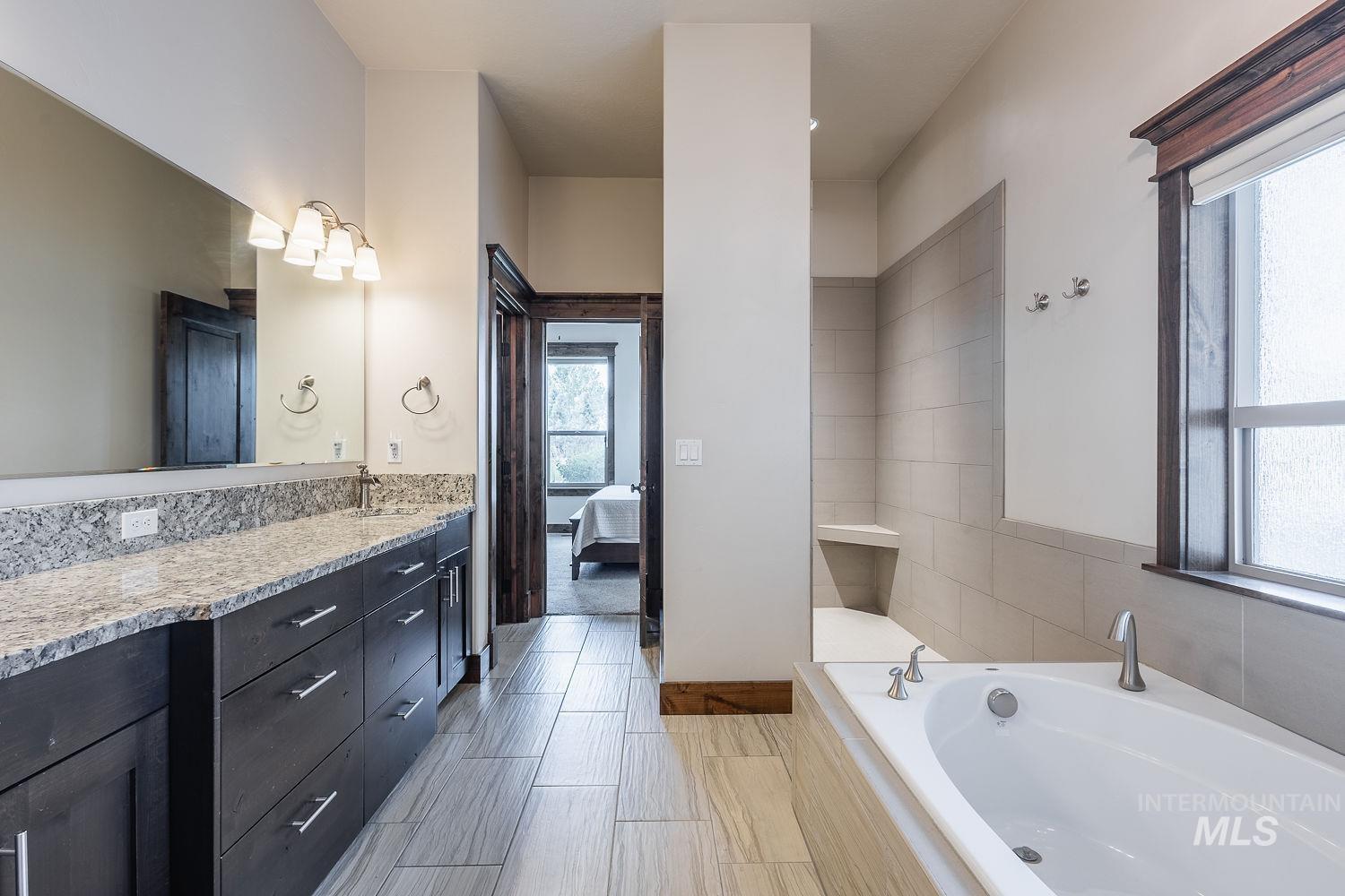 8077 Star Pass Ridge Road Nampa, ID 83686 - Photo 24 of 37 Bathroom featuring an elongated vanity with a light-toned countertop, a built-in soaking tub, a tiled shower with a bench, wood-finish flooring, and a large window