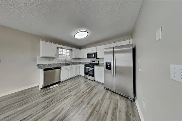 a kitchen with granite countertop a refrigerator oven a sink and dishwasher a oven with wooden floor