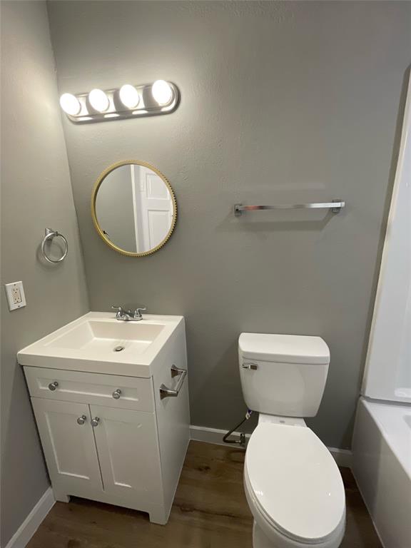 216 East Division Street Pilot Point, TX 76258 - Photo 15 of 17 Bathroom featuring wood-finish flooring, a white vanity with integrated sink, a round mirror, and an overhead four-bulb light fixture