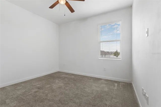 an empty room with chandelier fan and windows