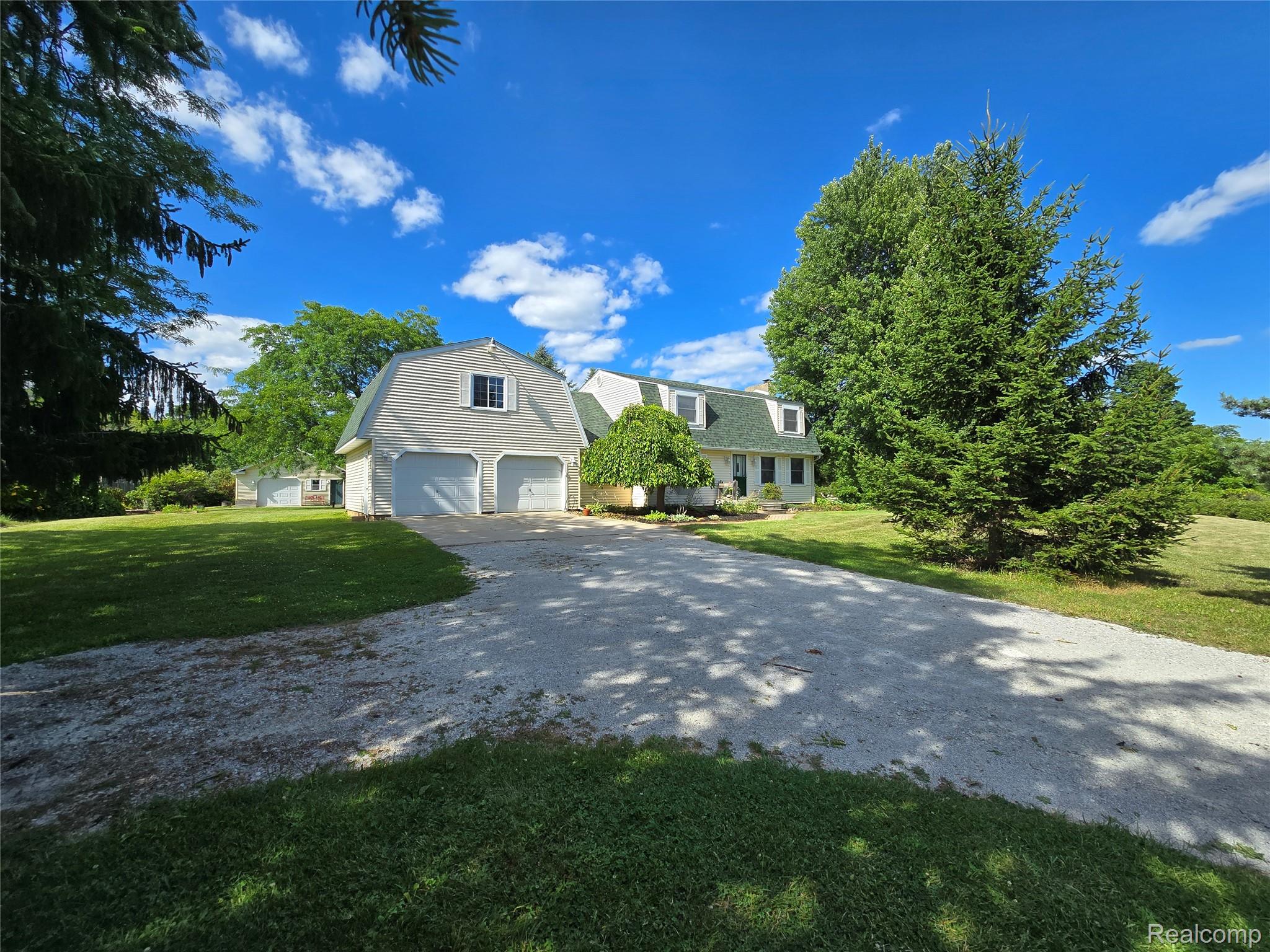 5282 McIntyre Road North Street, MI 48049 - Photo 10 of 53 Gravel driveway leading to a two-car garage with a gambrel roof and dormer window, surrounded by mature trees and natural landscaping