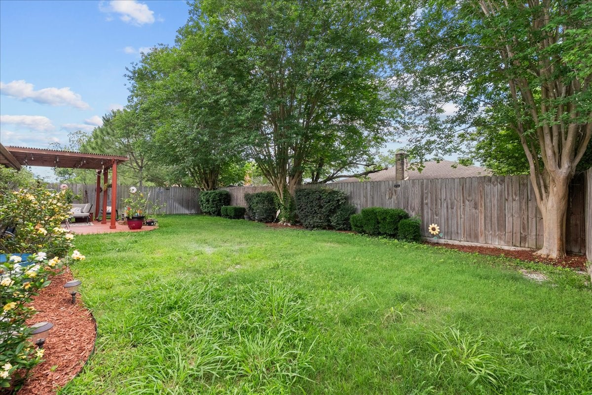 883 Silverpines Road Houston, TX 77062 - Photo 29 of 38 This backyard features a spacious, well-maintained lawn bordered by mature trees and a wooden fence, offering privacy and shade. A cozy patio area with seating and pergola adds a perfect spot for relaxation and outdoor gatherings.