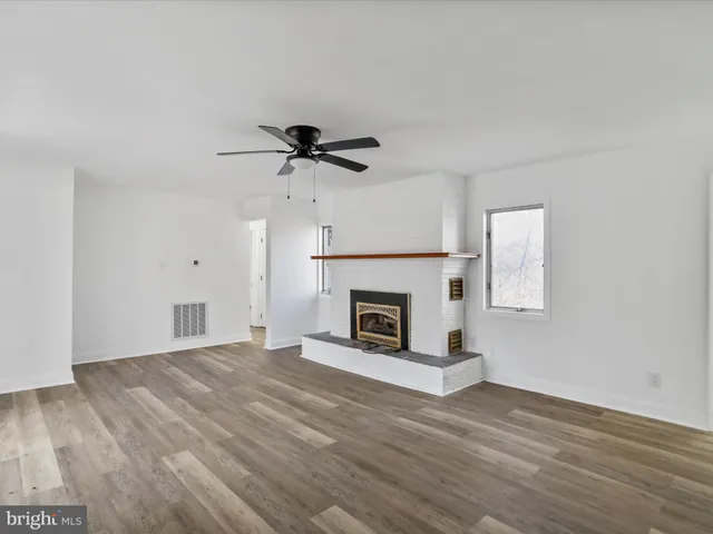 a view of a livingroom with a fireplace a ceiling fan and wooden floor
