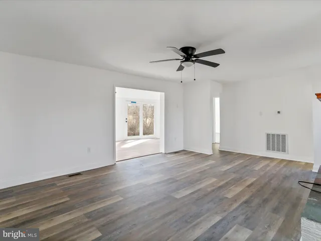 a view of an empty room with wooden floor and a ceiling fan