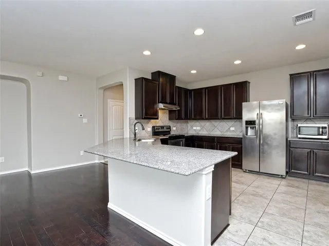 a kitchen with kitchen island granite countertop a sink a stove a refrigerator cabinets and a counter top space