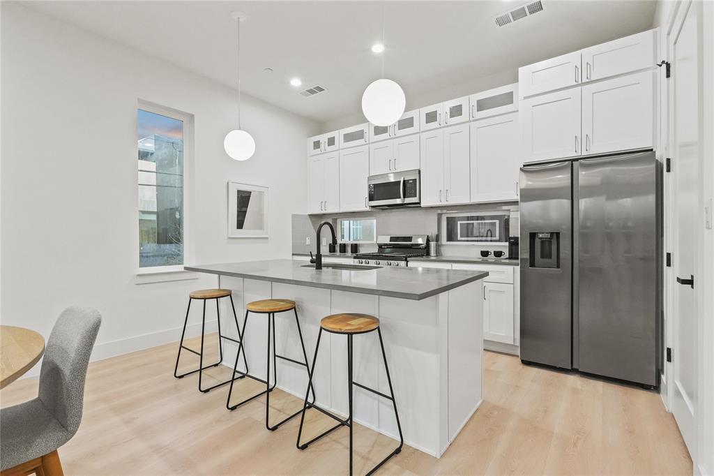 2031 North Prairie Avenue, Unit 101 Dallas, TX 75204 - Photo 10 of 23 Kitchen featuring stainless steel appliances, white cabinetry, light wood-style floors, glass insert cabinets, and a kitchen bar