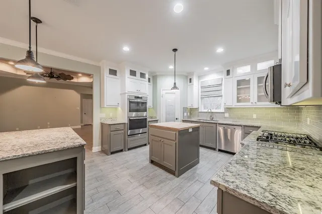 a large kitchen with stainless steel appliances granite countertop a stove a sink dishwasher a refrigerator and white cabinets with wooden floor
